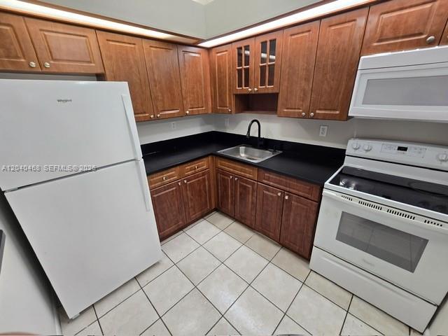 A kitchen features wood cabinets, white appliances, black countertops, and light-colored tile flooring — HIALEAH, FL