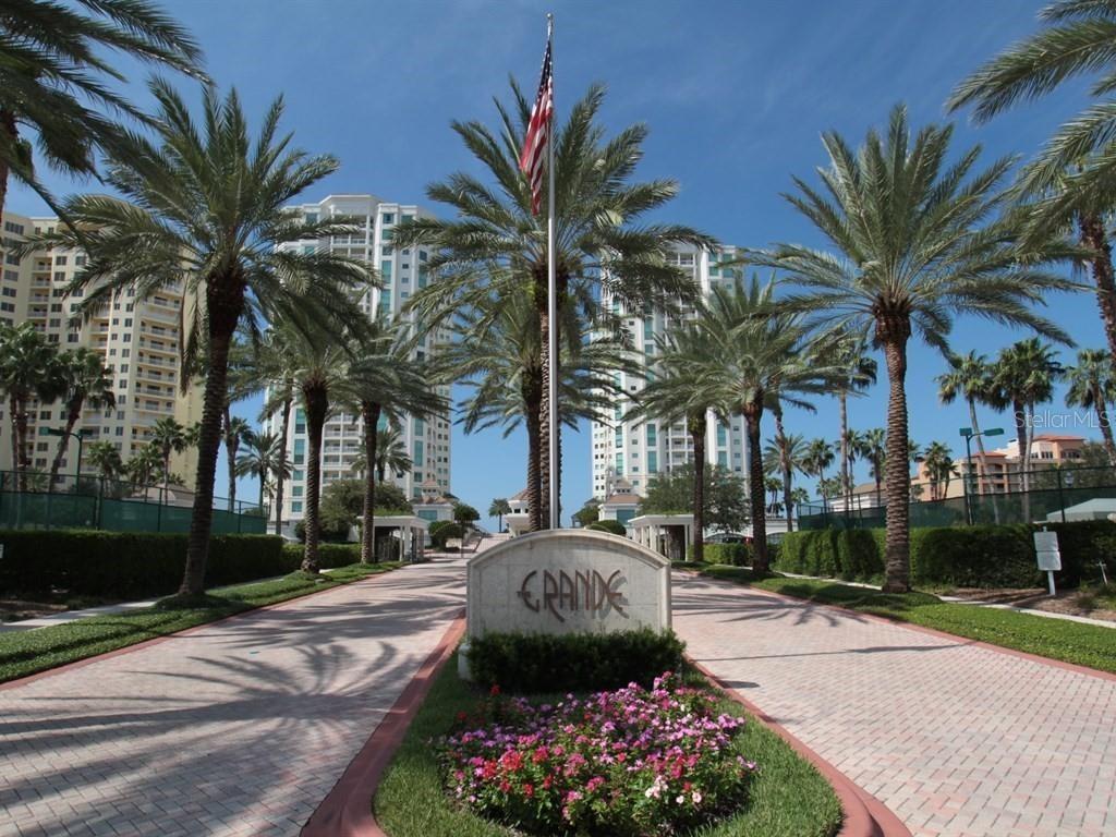 A stone monument sign labeled Grande stands at the entrance of a palm-lined driveway — 1180 GULF BOULEVARD UNIT 202, CLEARWATER BEACH, FL