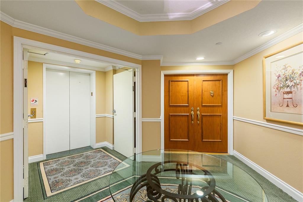An interior foyer features a glass-topped table, double wooden doors, and an elevator entrance — 1180 GULF BOULEVARD UNIT 202, CLEARWATER BEACH, FL