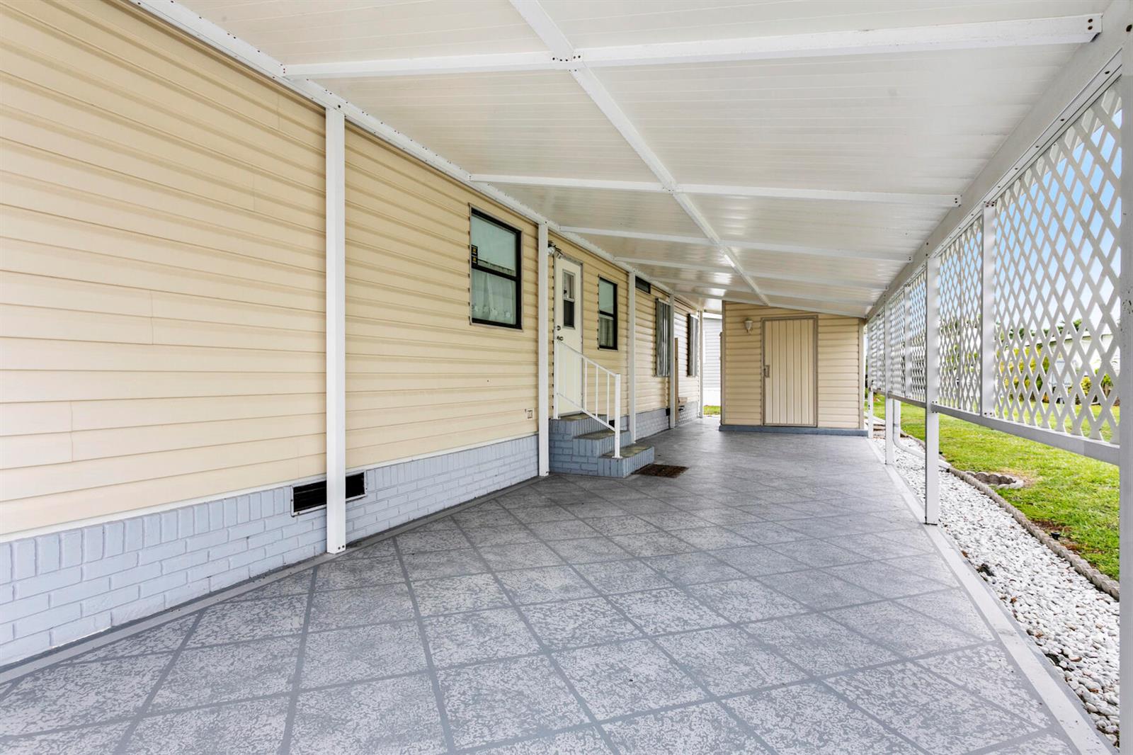 A covered carport with a patterned concrete floor, light siding, and a white lattice screen — 50018 Hacha Bay, Boynton Beach FL 33436, BOYNTON BEACH, FL