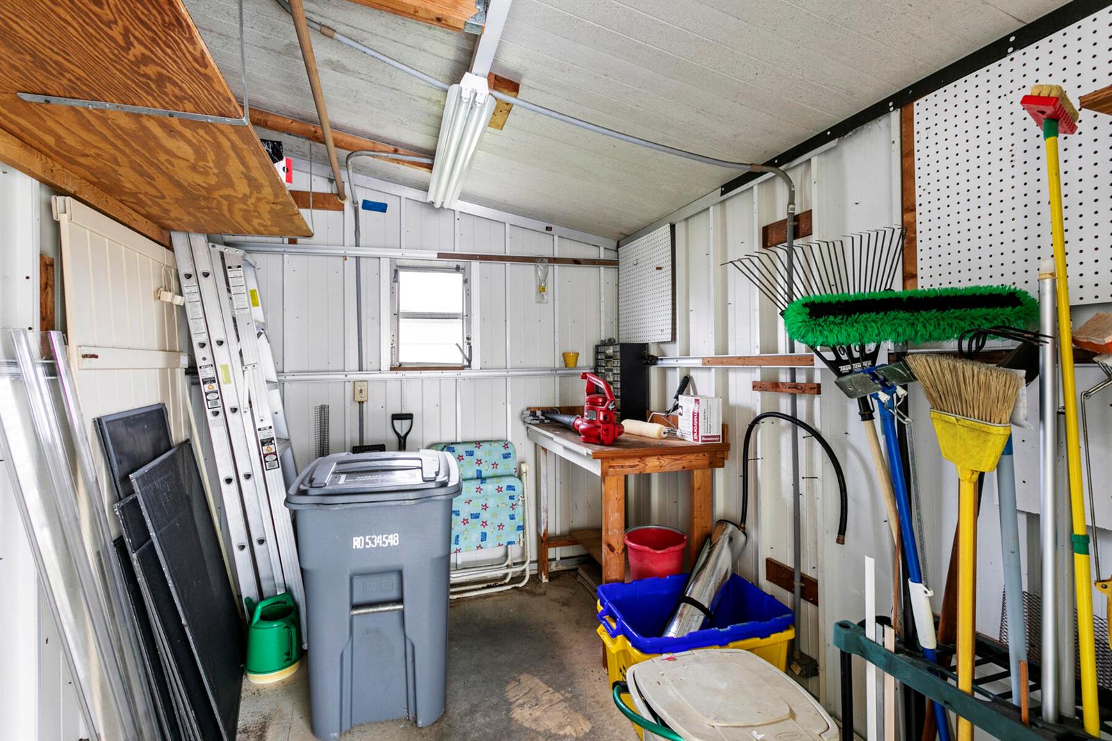 A cluttered storage shed with a workbench, tools, a trash bin, and a ladder — 50018 Hacha Bay, Boynton Beach FL 33436, BOYNTON BEACH, FL