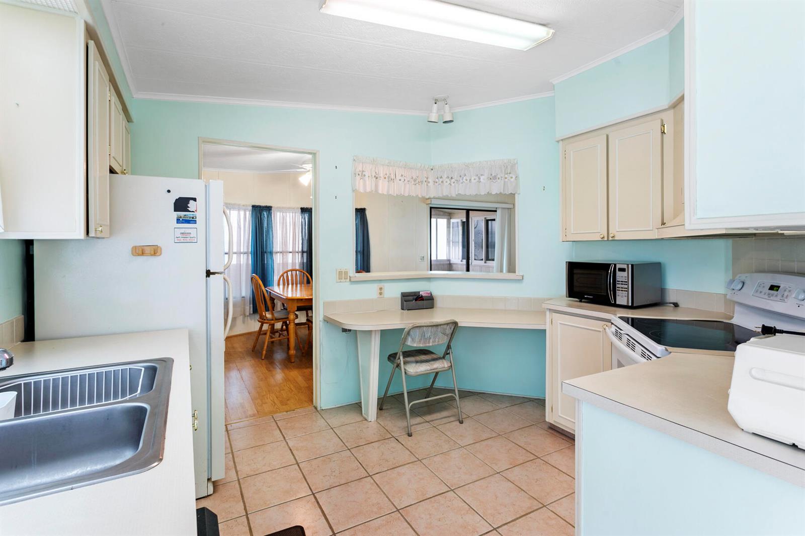 A kitchen with light blue walls, beige cabinets, tile flooring, and a built-in desk area — 50018 Hacha Bay, Boynton Beach FL 33436, BOYNTON BEACH, FL