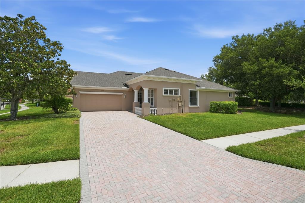 A single-story house with a beige stucco exterior, a paved driveway, and a two-car garage — 27325 MISTFLOWER DRIVE, WESLEY CHAPEL, FL