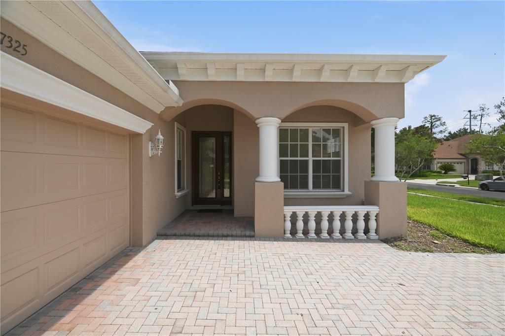 A tan house exterior features a paver driveway, a covered entryway, and white columns — 27325 MISTFLOWER DRIVE, WESLEY CHAPEL, FL