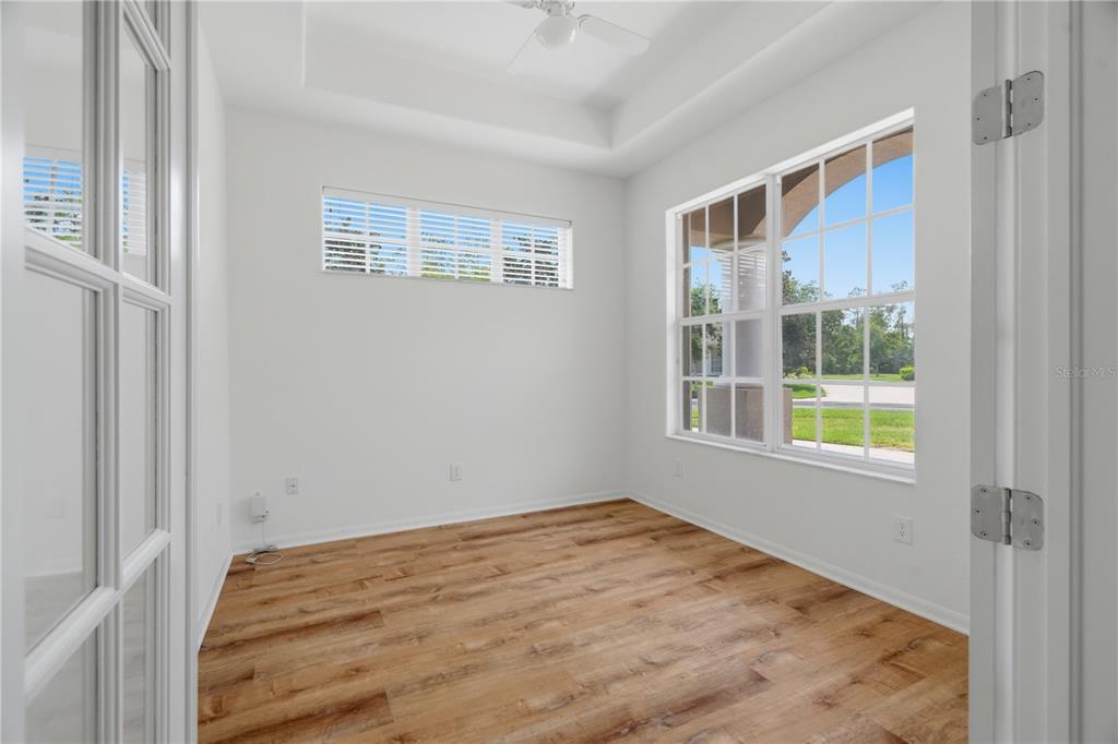 An empty room with wood-look flooring, white walls, a tray ceiling, and two windows — 27325 MISTFLOWER DRIVE, WESLEY CHAPEL, FL