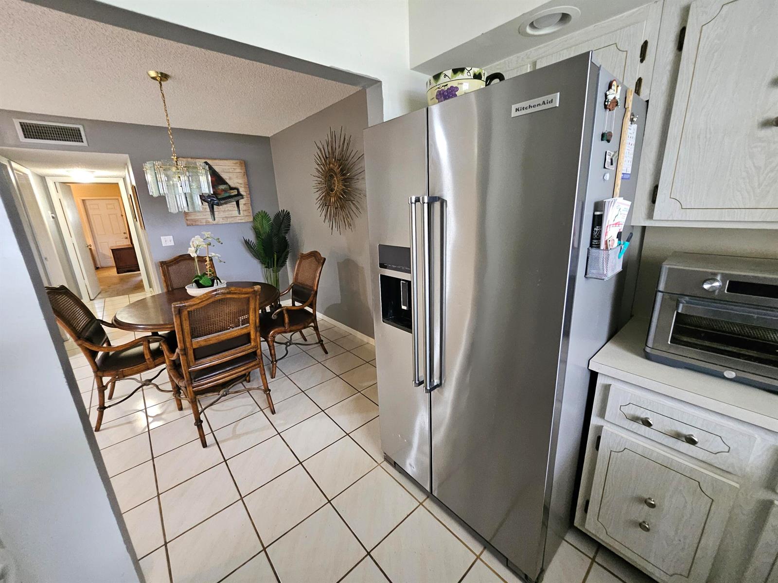 A stainless steel refrigerator stands in a kitchen next to a dining area with tile floors — 14628 Canalview Drive # A, Delray Beach FL 33484, DELRAY BEACH, FL