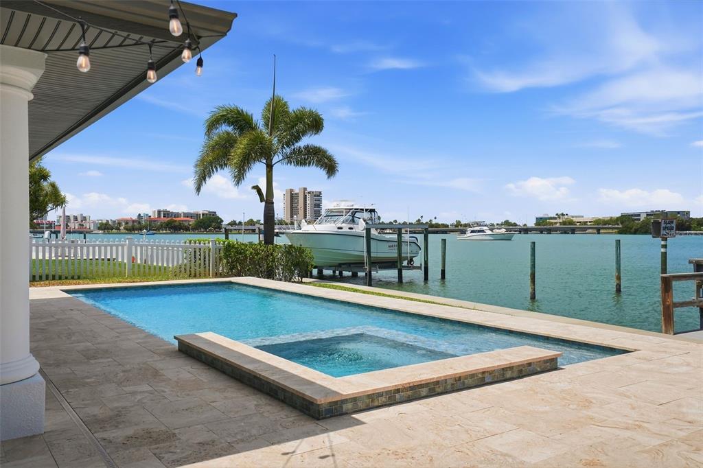 A swimming pool and spa overlook a waterfront area with a boat lift and palm tree — 7172 S SHORE DRIVE S, ST PETERSBURG, FL
