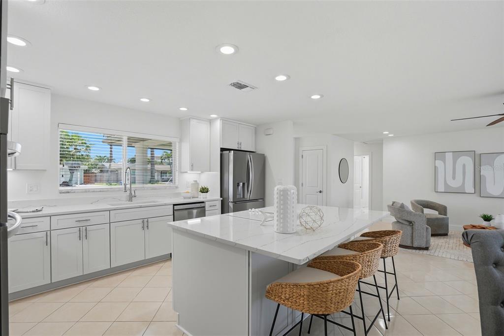 A modern white kitchen features a large quartz island with woven bar stools and cabinetry — 7172 S SHORE DRIVE S, ST PETERSBURG, FL