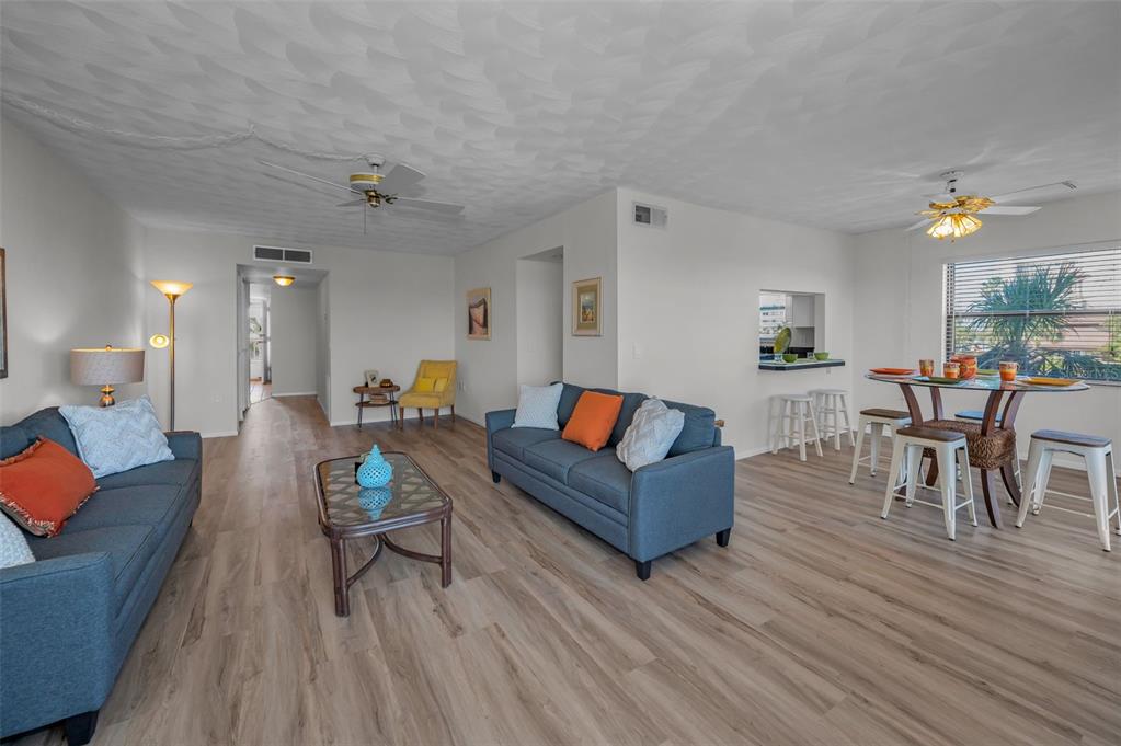 A living room and dining area with blue sofas, wood-look flooring, and a ceiling fan — 19451 GULF BOULEVARD UNIT 301, INDIAN SHORES, FL