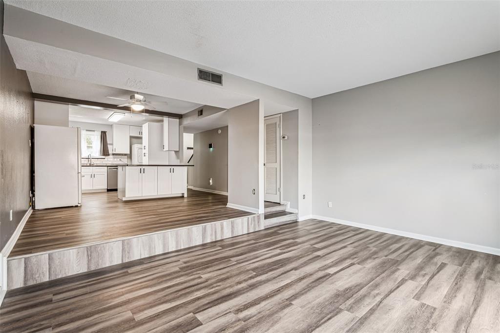 A living room with wood-look flooring features a raised kitchen area with white cabinetry — 200 SAINT ANDREWS BOULEVARD UNIT 2904, WINTER PARK, FL