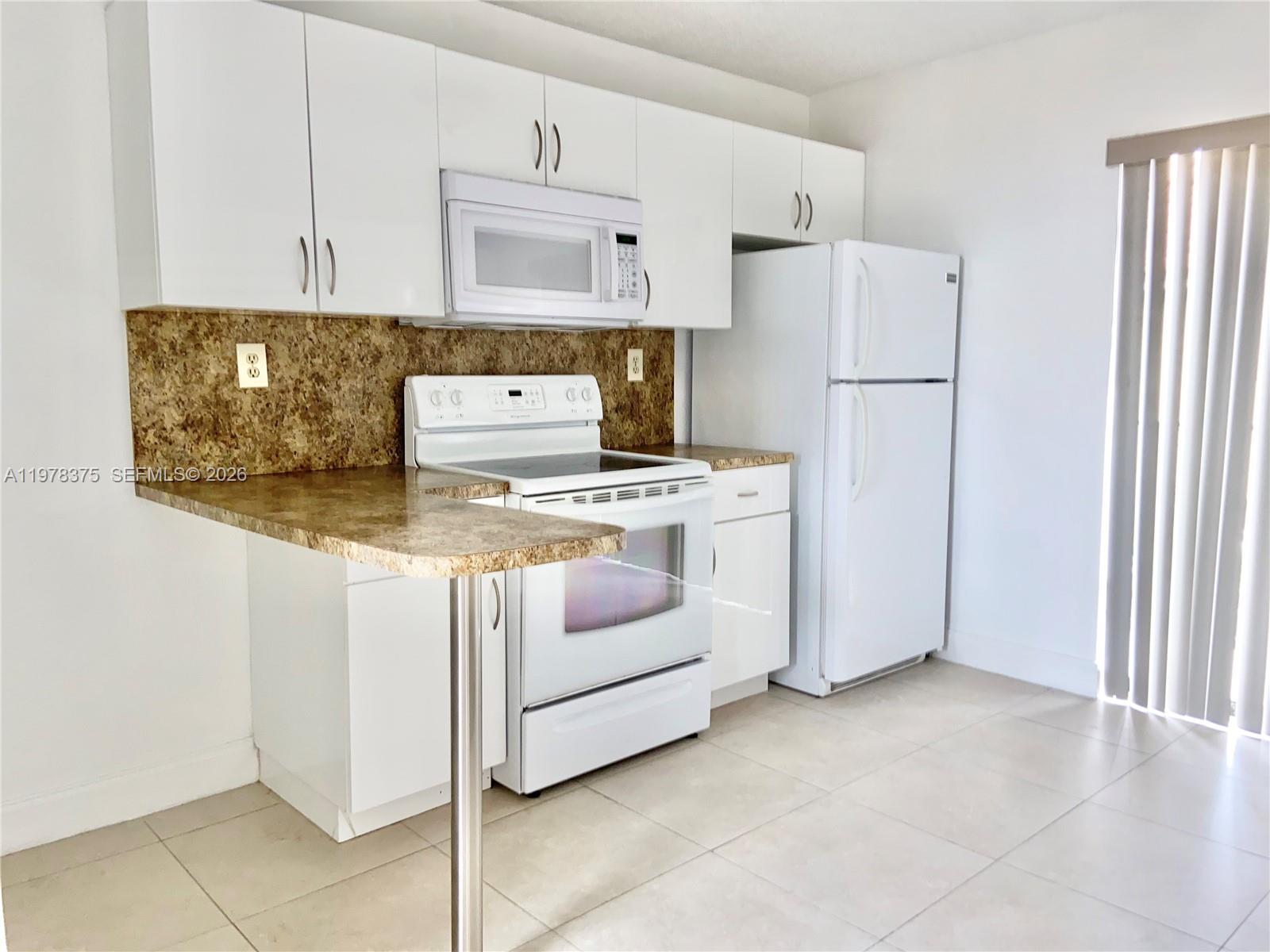 A kitchen features white cabinets, white appliances, and a brown speckled countertop with a breakfast bar — 2740 W 62nd St # 203, Hialeah FL 33016, HIALEAH, FL