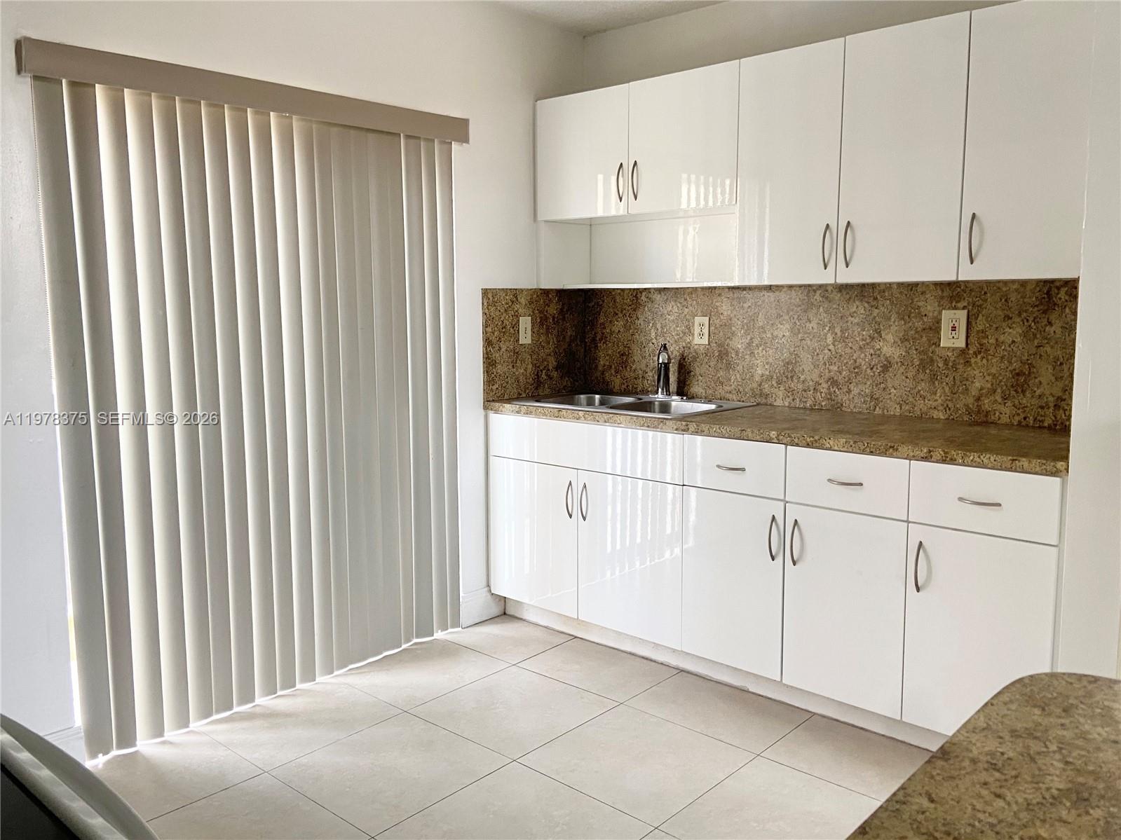 A kitchen features white cabinets, a speckled countertop, a stainless steel sink, and vertical blinds — 2740 W 62nd St # 203, Hialeah FL 33016, HIALEAH, FL