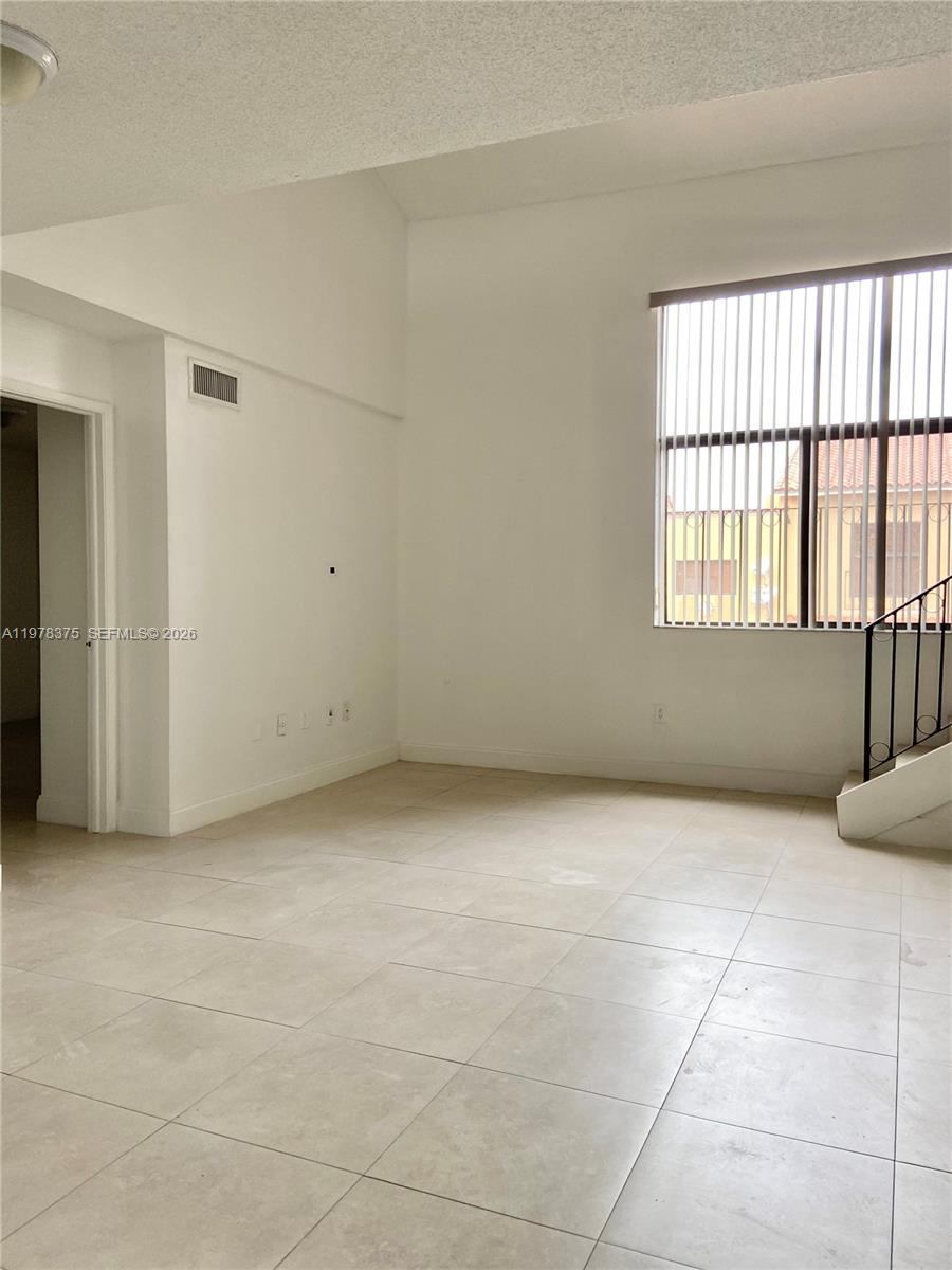 An empty room features white walls, light-colored tile flooring, a high ceiling, and a large window — 2740 W 62nd St # 203, Hialeah FL 33016, HIALEAH, FL