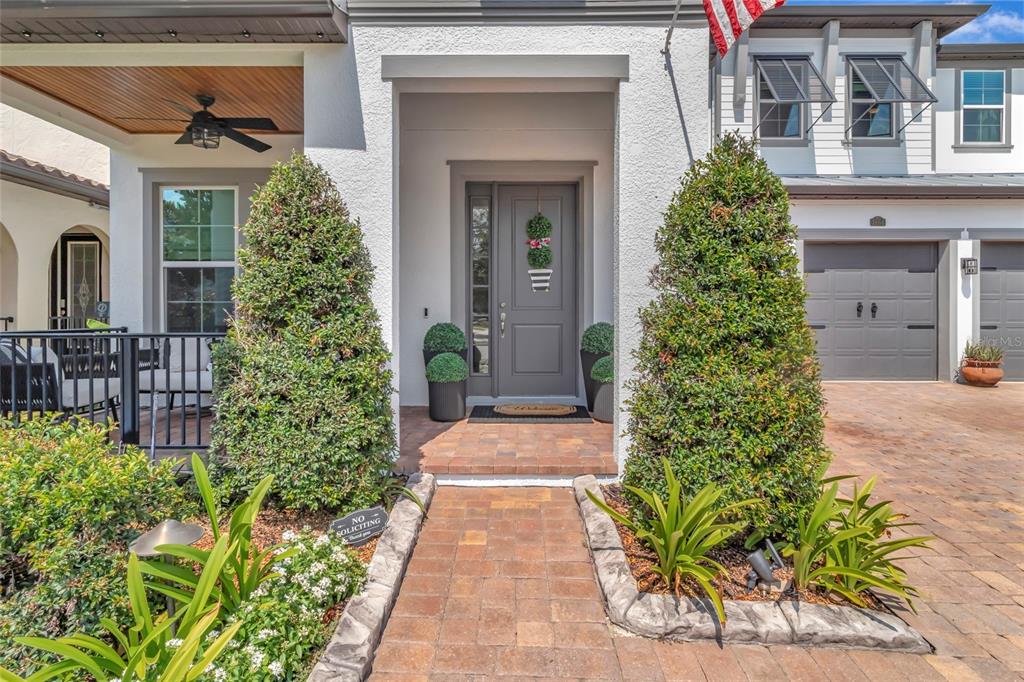 A front entrance with a gray door, stone walkway, and two large topiaries in planters — 1664 HOLCOMB CREEK ST., WINTER GARDEN, FL