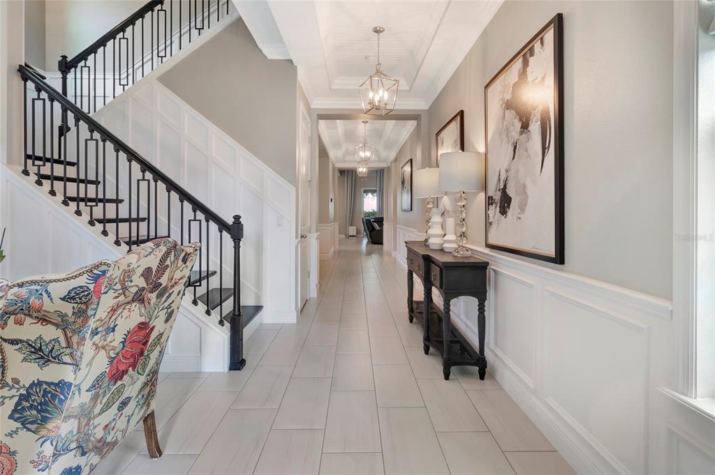 A bright entryway features a staircase with black railings, a long hallway, and tile flooring — 1664 HOLCOMB CREEK ST., WINTER GARDEN, FL