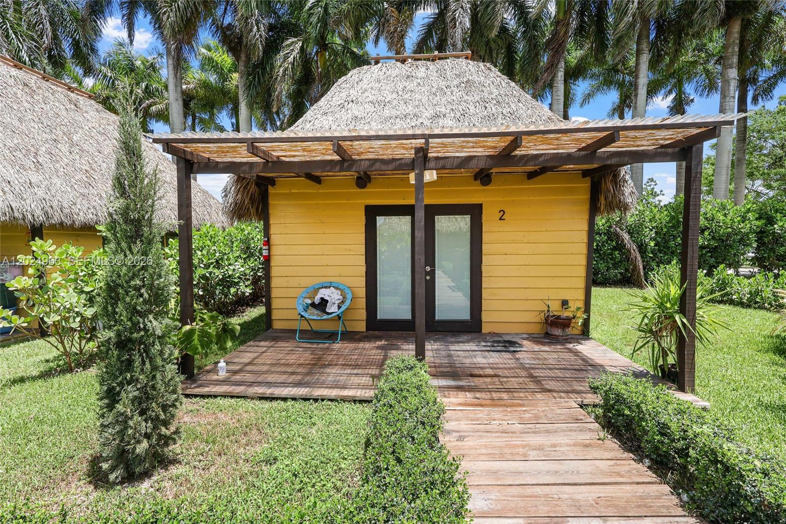 A yellow cabin with a thatched roof and a wooden deck sits on a lawn — 14701 SW 199th Ave, Miami FL 33196, MIAMI, FL