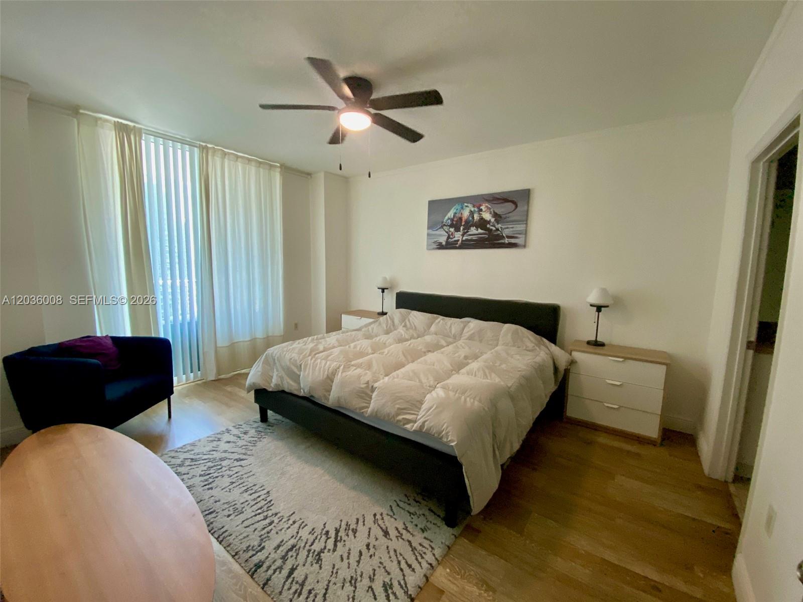 A bedroom features a bed with a white comforter, a dark chair, and wood flooring — 1250 S Miami Ave # 1312, Miami FL 33130, MIAMI, FL