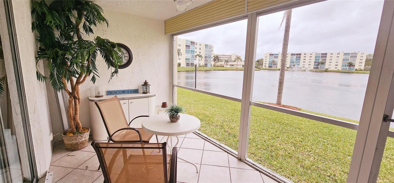 A screened-in patio features tile flooring, a small table with chairs, and a lake view — 121 SE 3rd Avenue # 106, Dania Beach FL 33004, DANIA BEACH, FL