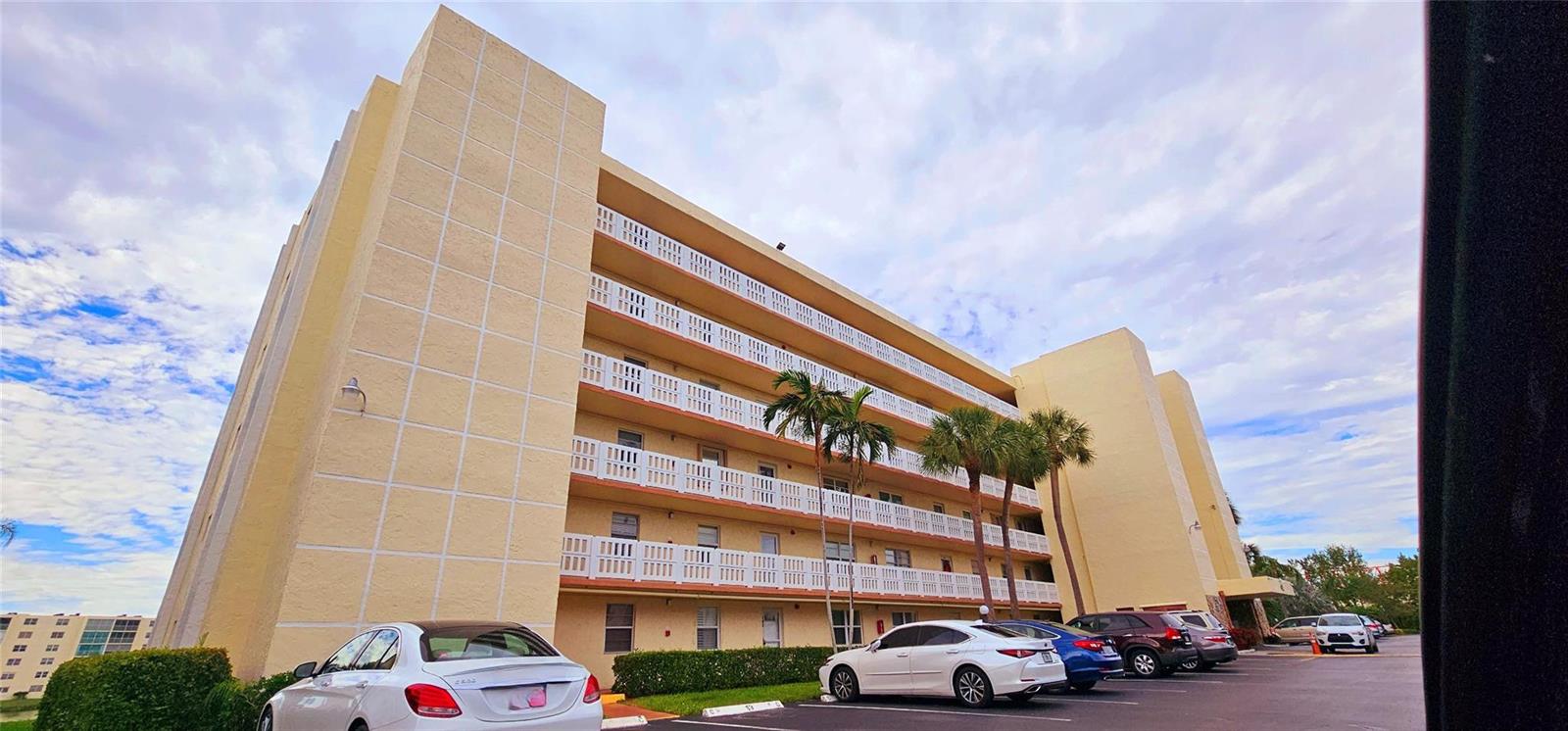 A low-angle exterior view of a multi-story apartment building with a parking lot in front — 121 SE 3rd Avenue # 106, Dania Beach FL 33004, DANIA BEACH, FL