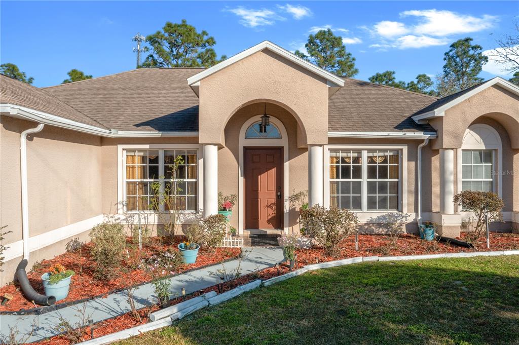 The exterior of a tan stucco house features a covered entryway with white columns — 27 VINCA STREET, HOMOSASSA, FL