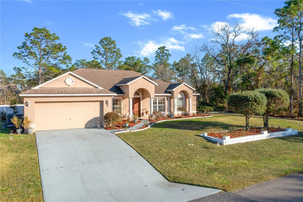 A single-story tan house with a two-car garage and a front lawn with landscaping — 27 VINCA STREET, HOMOSASSA, FL