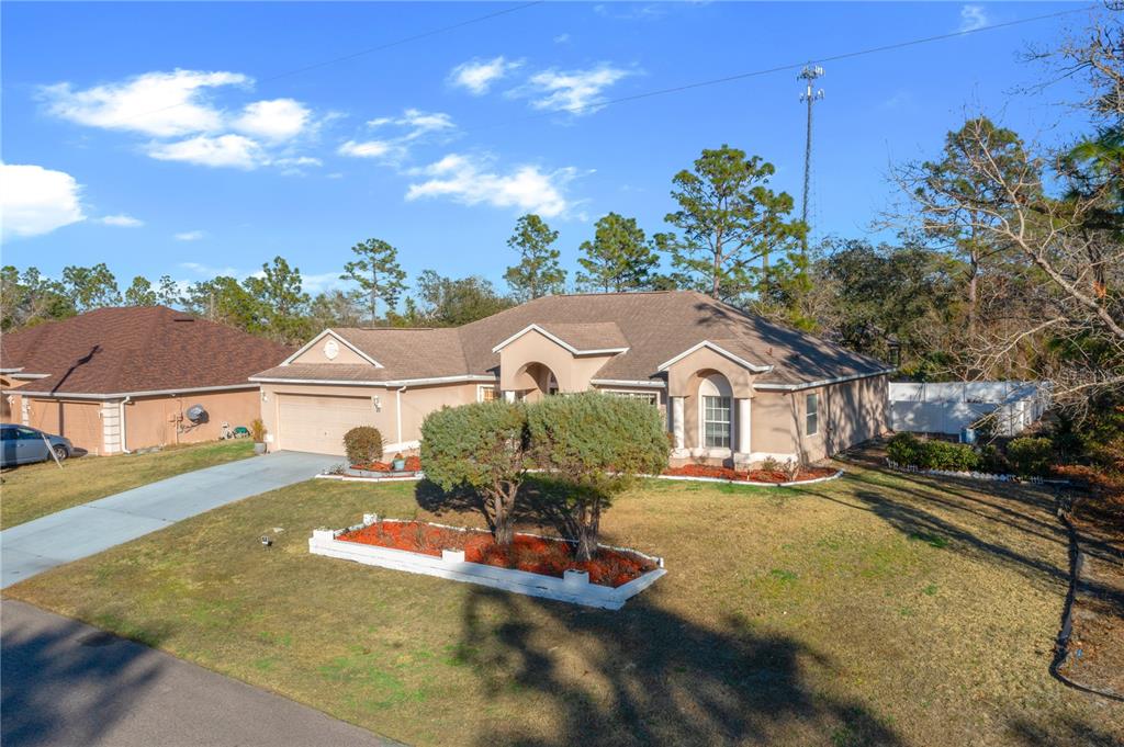A single-story tan house with a two-car garage and a front yard with landscaping — 27 VINCA STREET, HOMOSASSA, FL