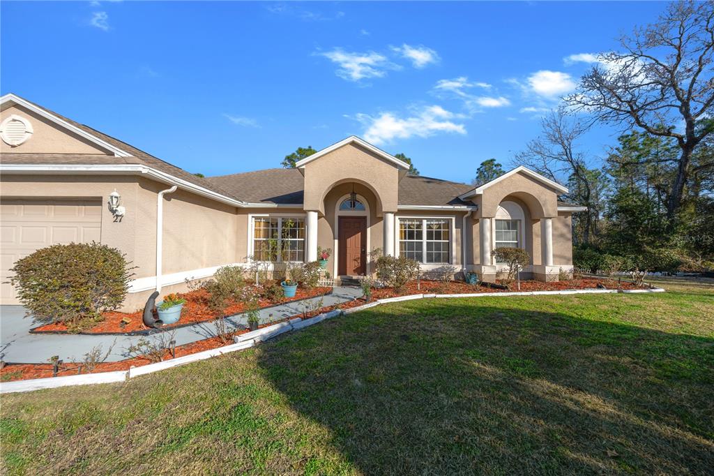 A single-story tan house with a brown roof, arched entryway, and a front lawn — 27 VINCA STREET, HOMOSASSA, FL