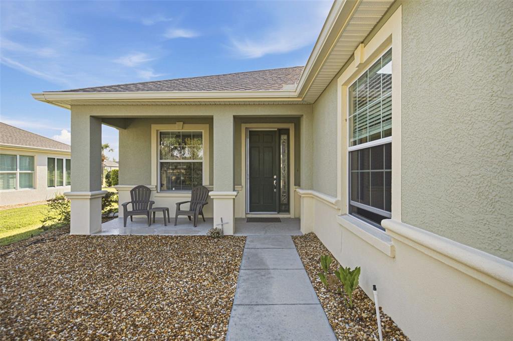 A concrete walkway leads to the covered front porch of a light green stucco house — 6951 SW 94TH COURT, OCALA, FL