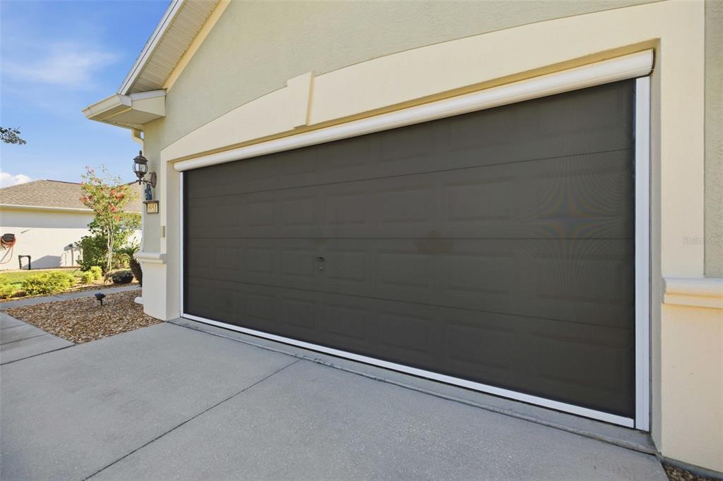 A residential garage door features a dark, retractable mesh screen covering the opening — 6951 SW 94TH COURT, OCALA, FL