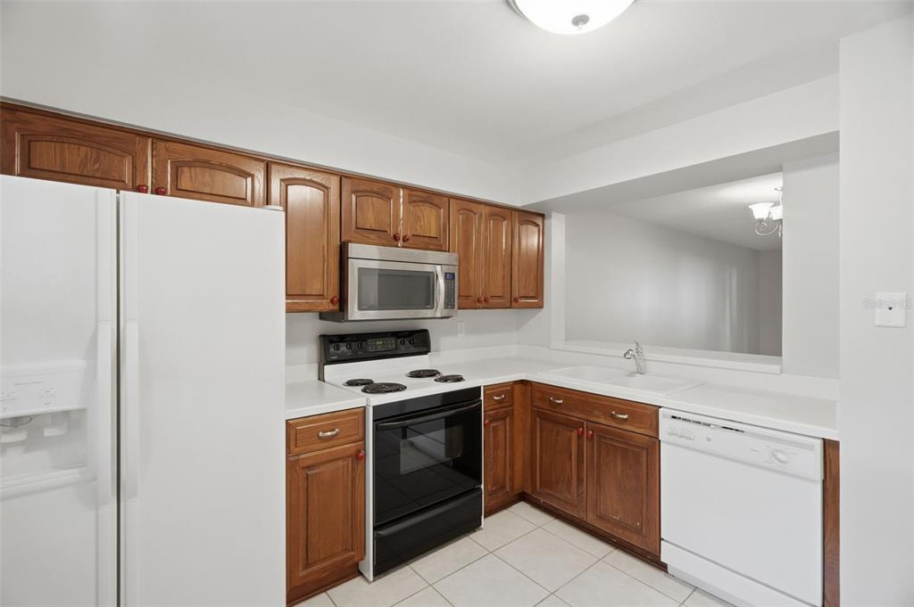 A kitchen features wood cabinets, white countertops, and white appliances including a refrigerator and dishwasher — 3399 MERMOOR DRIVE UNIT 105, PALM HARBOR, FL