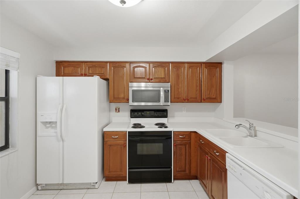 A kitchen features wood cabinets, a white refrigerator, a black stove, and a white sink — 3399 MERMOOR DRIVE UNIT 105, PALM HARBOR, FL