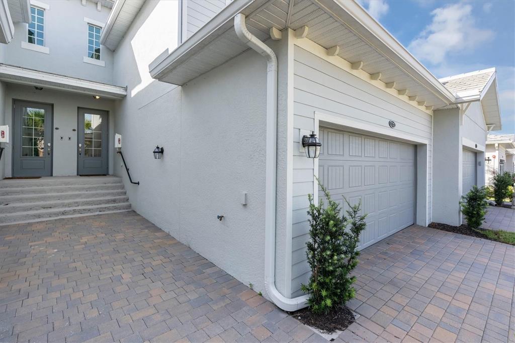 The exterior of a multi-unit building features gray garage doors, a paved driveway, and stairs — 14680 SYCAMORE COURT UNIT 3722, PUNTA GORDA, FL