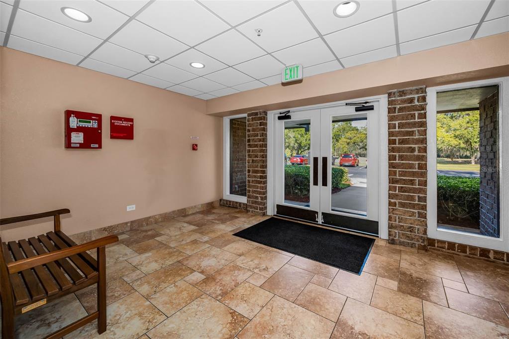 A tiled lobby features a wooden bench, a fire alarm box, and double glass exit doors — 36750 US HIGHWAY 19 N UNIT 28-2017, PALM HARBOR, FL