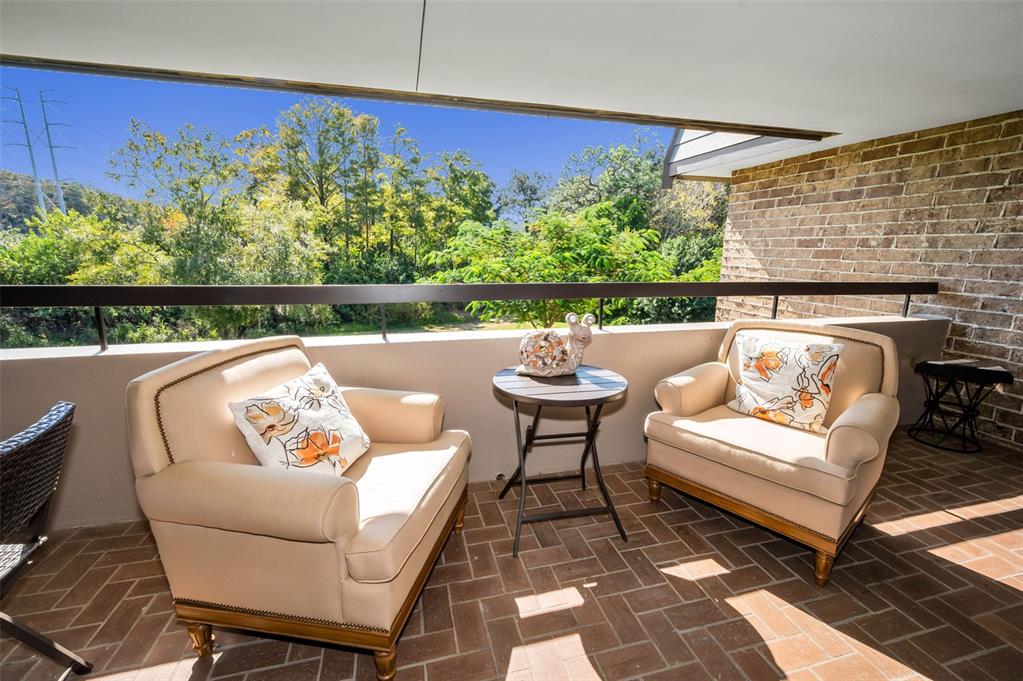 A covered balcony features two beige armchairs, a small round table, and brick flooring — 36750 US HIGHWAY 19 N UNIT 28-2017, PALM HARBOR, FL