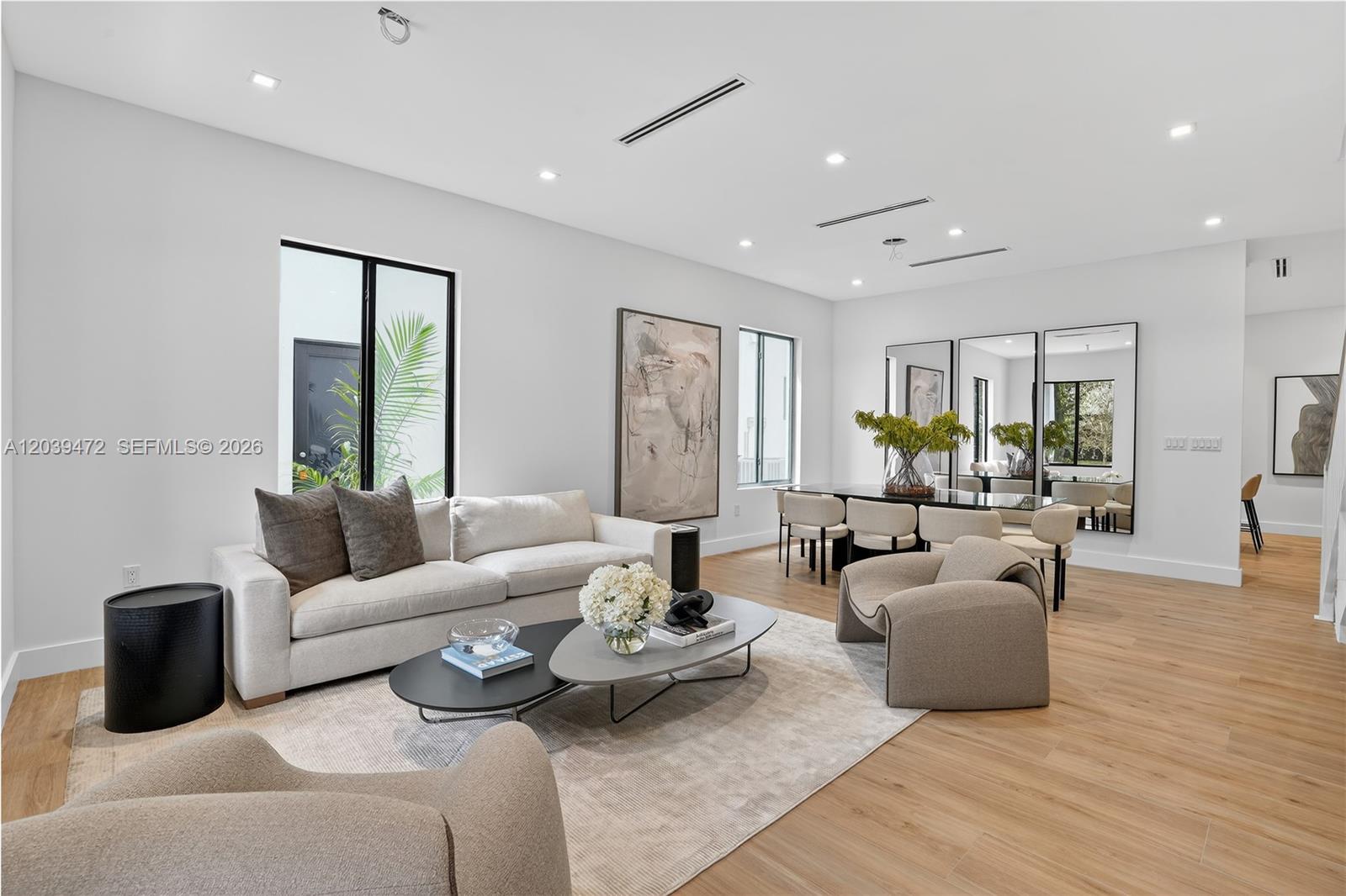 A modern living and dining area features light wood floors, neutral furniture, and large mirrors — 7212 SW 52nd Ct, Miami FL 33143, MIAMI, FL