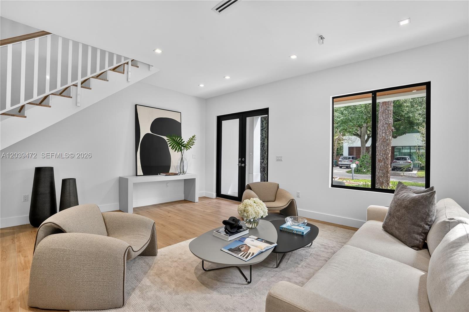 A modern living room features a staircase, neutral furniture, a coffee table, and large windows — 7212 SW 52nd Ct, Miami FL 33143, MIAMI, FL