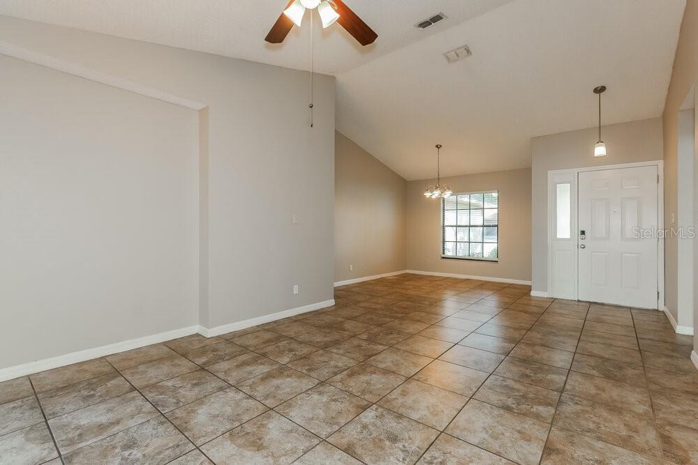 A spacious room with light gray walls, tiled flooring, a vaulted ceiling, and an entryway — 1424 COVINGTON COURT, LAKE WALES, FL