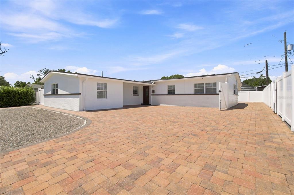 A white single-story house features a brick-paved driveway and a gravel front yard — 6033 AMBASSADOR DRIVE, TAMPA, FL