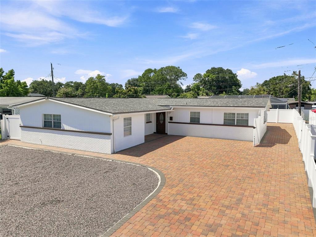 A white house with a gravel driveway and a white vinyl fence under a blue sky — 6033 AMBASSADOR DRIVE, TAMPA, FL