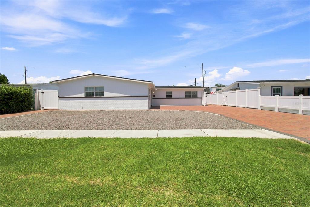 The exterior of a white house features a brick base, a gravel driveway, and white fencing — 6033 AMBASSADOR DRIVE, TAMPA, FL