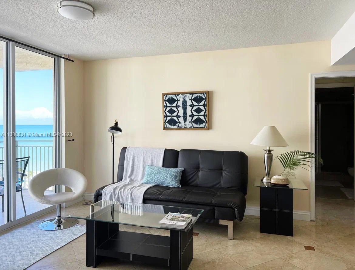 A living room features a black sofa, glass coffee table, and a balcony with ocean views — 2080 S Ocean Dr # 806, Hallandale Beach FL 33009, HALLANDALE BEACH, FL