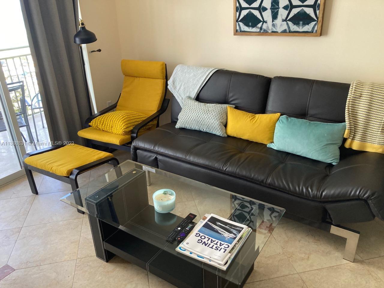 A living room features a black sofa, a yellow chair with ottoman, and a glass table — 2080 S Ocean Dr # 806, Hallandale Beach FL 33009, HALLANDALE BEACH, FL