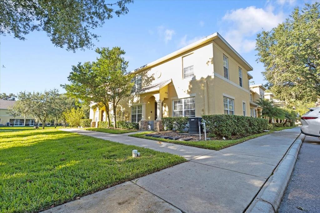 A two-story yellow stucco townhouse exterior with a sidewalk and surrounding green lawn — 37554 DALIHA TERRACE, ZEPHYRHILLS, FL
