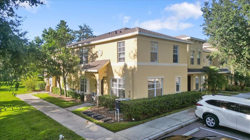 A two-story tan stucco townhouse with a sidewalk and a parked white SUV — 37554 DALIHA TERRACE, ZEPHYRHILLS, FL