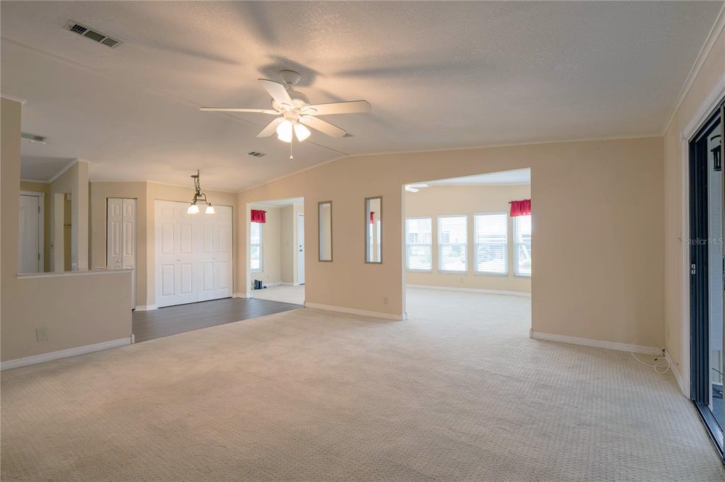 A spacious living room with beige carpet, a ceiling fan, and an adjacent sunroom — 5910 MAJESTIC WAY, PALMETTO, FL