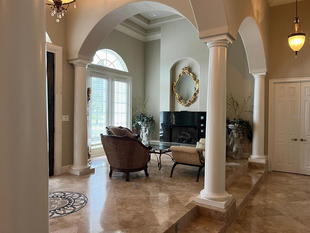A formal living room features marble floors, arched columns, and a fireplace with a mirror — 6354 CARTMEL LANE, WINDERMERE, FL