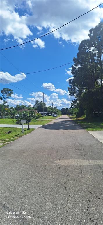 A paved residential street stretches into the distance under a bright, partly cloudy sky — 526 OSAGE AVENUE S, LEHIGH ACRES, FL