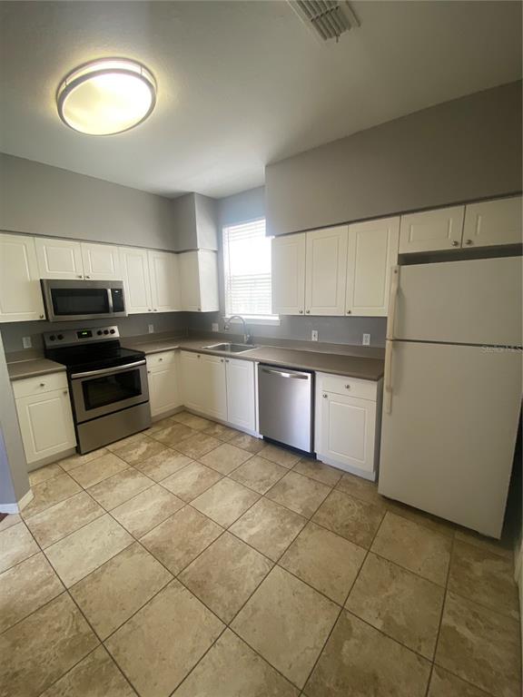A kitchen features white cabinets, stainless steel appliances, a white refrigerator, and tiled flooring — 4009 SAND PALM COURT, TAMPA, FL