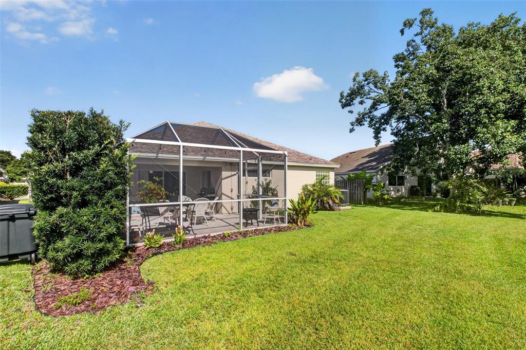 A backyard features a screened-in patio attached to a house with a large green lawn — 1763 SUN GAZER DRIVE, ROCKLEDGE, FL