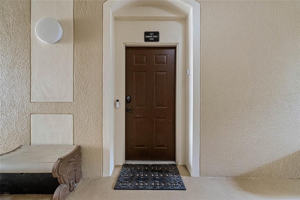 A brown front door with a keypad lock and a doormat sits in a hallway — 7671 COMROW STREET UNIT 202, KISSIMMEE, FL